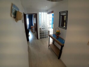 A hallway with a wooden floor, a blue console table with a basket of flowers, a decorative mirror, and a wall-mounted picture. - Algarve, modern T1 apartment with/balcony, Quarteira (Quarteira)