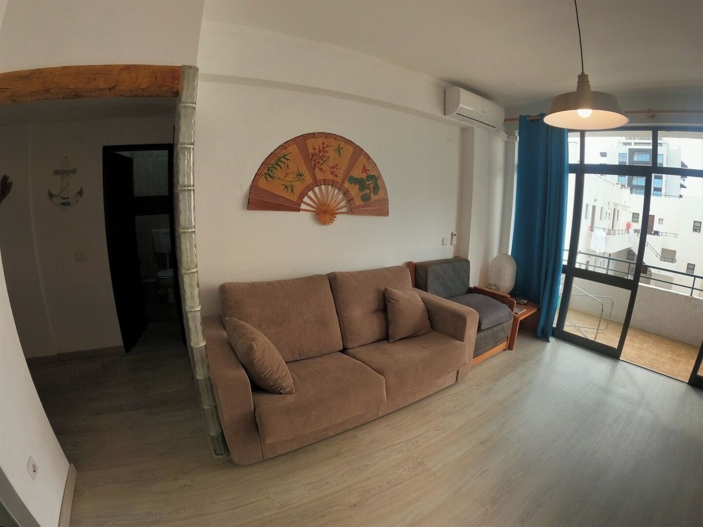 Una sala de estar con un sofá marrón, un abanico decorativo y vistas a través de un gran ventanal.
