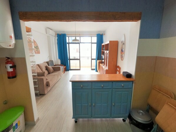 A living room with a sofa, a coffee table, and a kitchen area with a blue cabinet and a countertop. - Algarve, modern T1 apartment with/balcony, Quarteira (Quarteira)