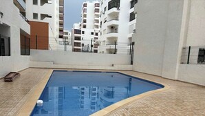 Ein rechteckiger Pool mit Fliesenboden, umgeben von weißen Wänden und einem Metallzaun.