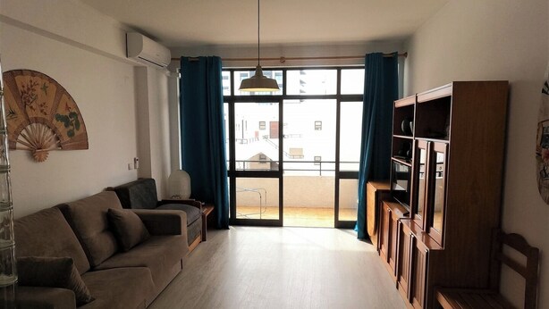 Ein Wohnzimmer mit einer Couch, einem Holzschrank, einer Pendelleuchte und einem großen Fenster mit Vorhängen.