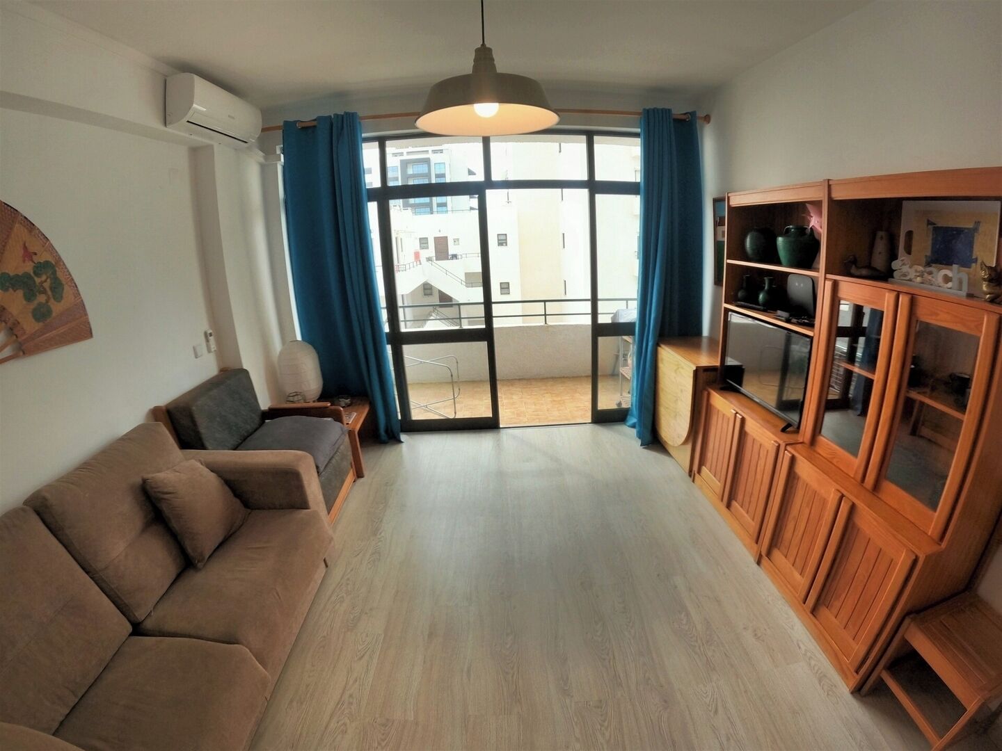 A living room with a sofa, a cabinet, a ceiling fan, and a view through a glass door.