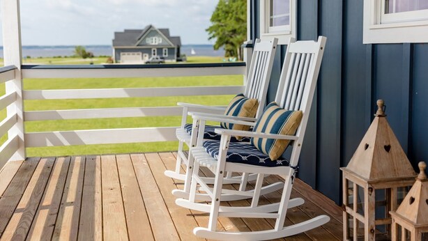 A wooden deck with rocking chairs and a lantern, overlooking a grassy area and a house. - Dockside - Picture Perfect Home - Gorgeous Views! (Arapahoe)