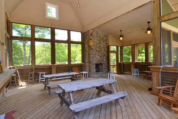 A covered outdoor dining area with wooden benches and picnic tables, large windows, and a stone fireplace. - Sugar Shack - Rustic charm meets modern amenities! (Arapahoe)