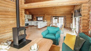 A cozy log cabin interior with a central living area featuring a sofa and a table, a kitchen with a stove, and a dining area with chairs. - 3 bedroom stunning home in Samsø (Samsø)