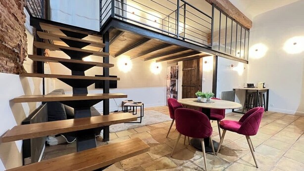 A dining area with a wooden staircase, a round table, and red chairs. - La Romance - Loft Ancien au coeur de Toulouse (Toulouse)