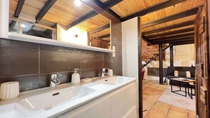 A bathroom with a large white sink, two faucets, and a mirror. There is a wooden ceiling and a staircase leading to another room. - La Romance - Loft Ancien au coeur de Toulouse (Toulouse)