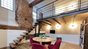 A dining area with a round table, red chairs, and a brick wall. - La Romance - Loft Ancien au coeur de Toulouse (Toulouse)