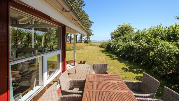 A covered outdoor seating area with wicker furniture and a wooden table, overlooking a grassy landscape with trees and a distant view. - 2 bedroom lovely home in Samsø (Samsø)