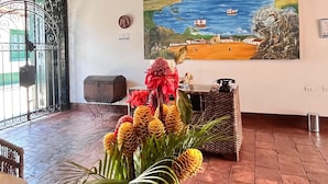A reception area with a large painting of a coastal scene, a reception desk, and a decorative plant centerpiece. - Camino a Santa Fe (Guaduas)