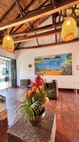 Un área de recepción con un cuadro de gran tamaño que muestra una escena costera, un mostrador de recepción y un centro de mesa decorativo con plantas.