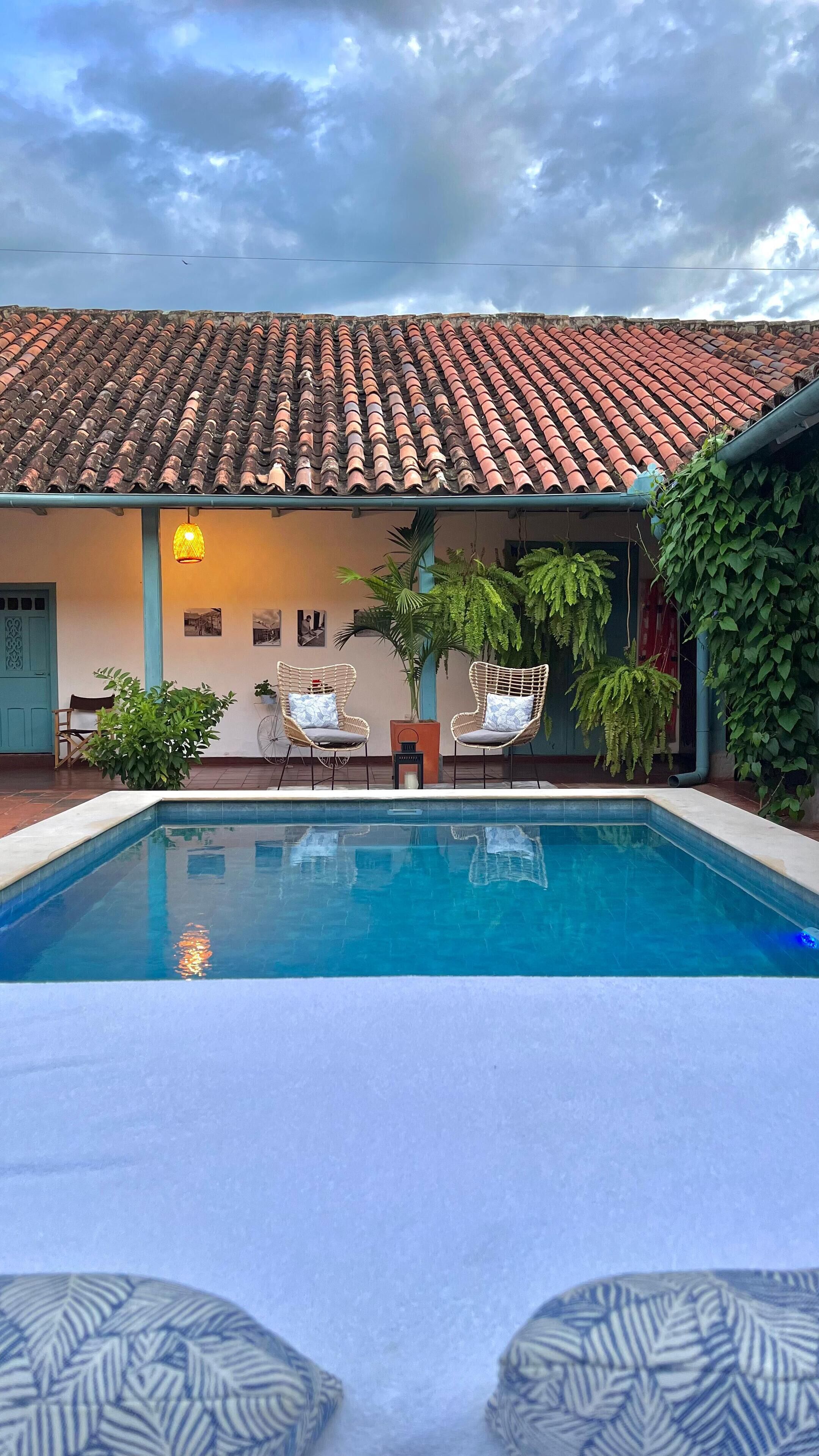 Une piscine agrémentée de deux fauteuils en osier et d’une petite table, le tout entouré de verdure et surmonté d’un toit en tuiles.
