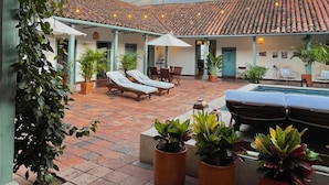 A covered outdoor area with a tiled roof, potted plants, lounge chairs, and a pool. - Camino a Santa Fe (Guaduas)