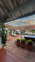 Un espacio exterior cubierto con techo de baldosas, plantas en macetas, sillones de descanso y una piscina.
