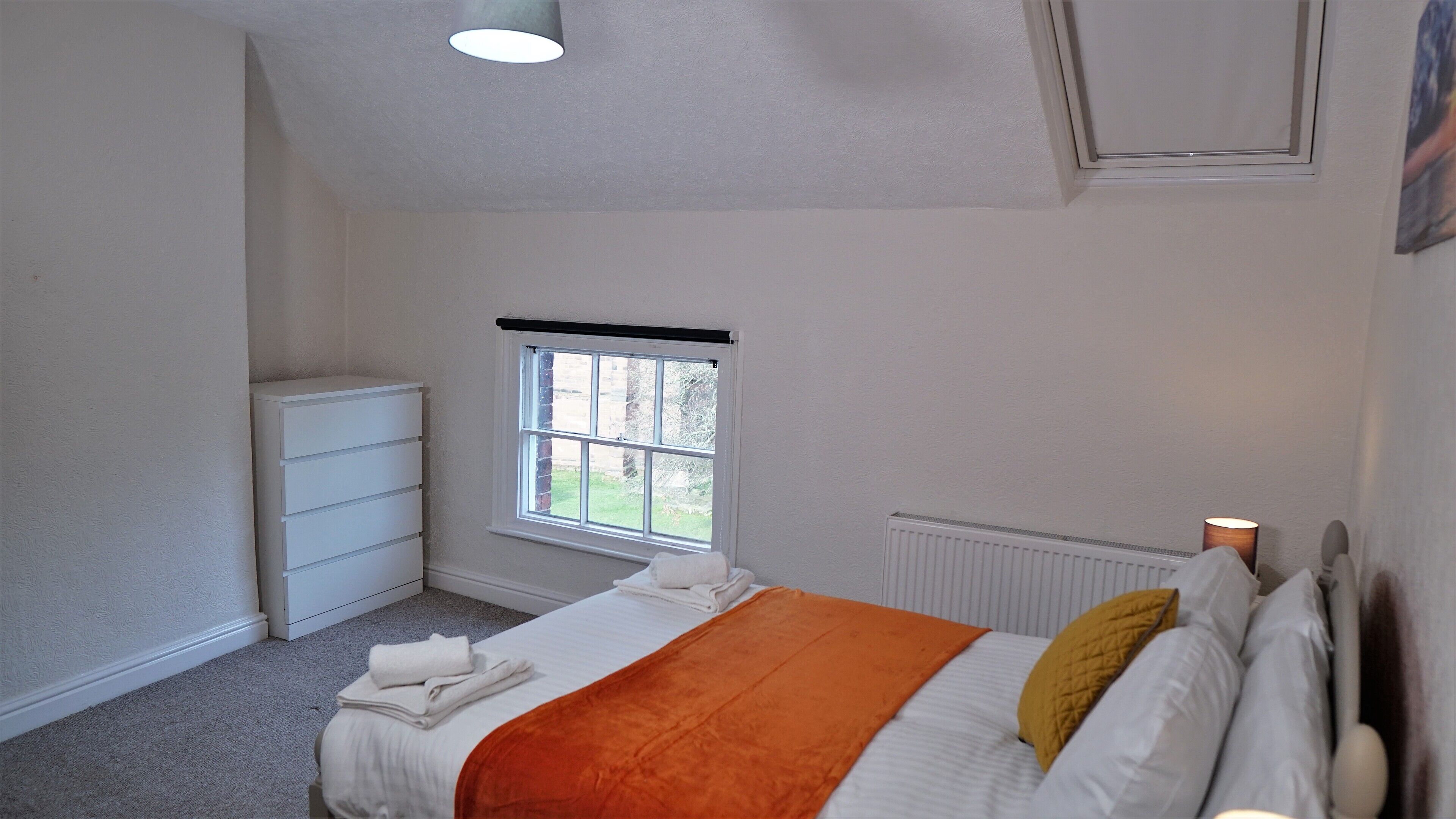 A bedroom with a bed, a radiator, a window, and a white wardrobe.