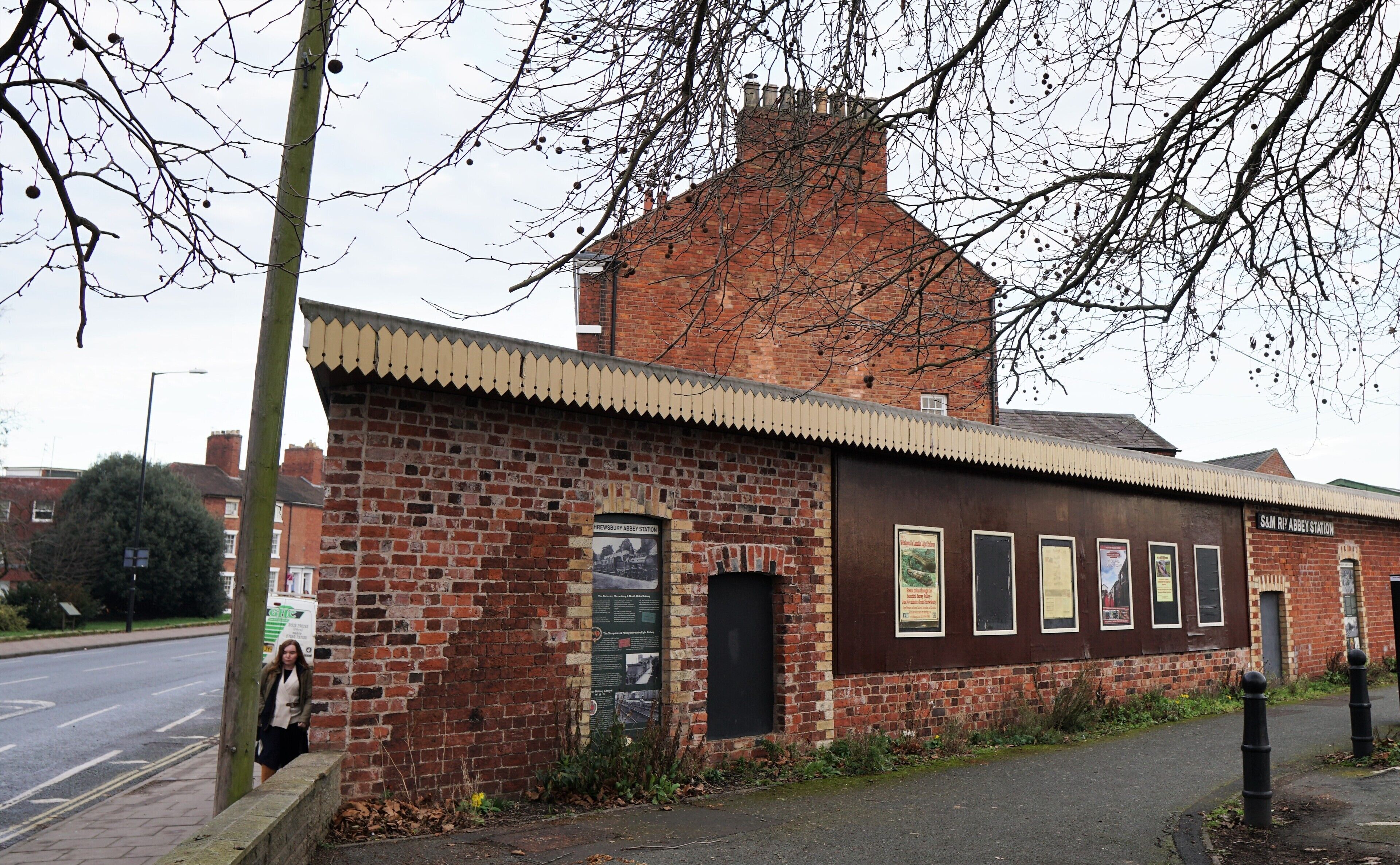 A brick building with a traditional design, featuring a large chimney and a small attached structure with multiple informational posters.
