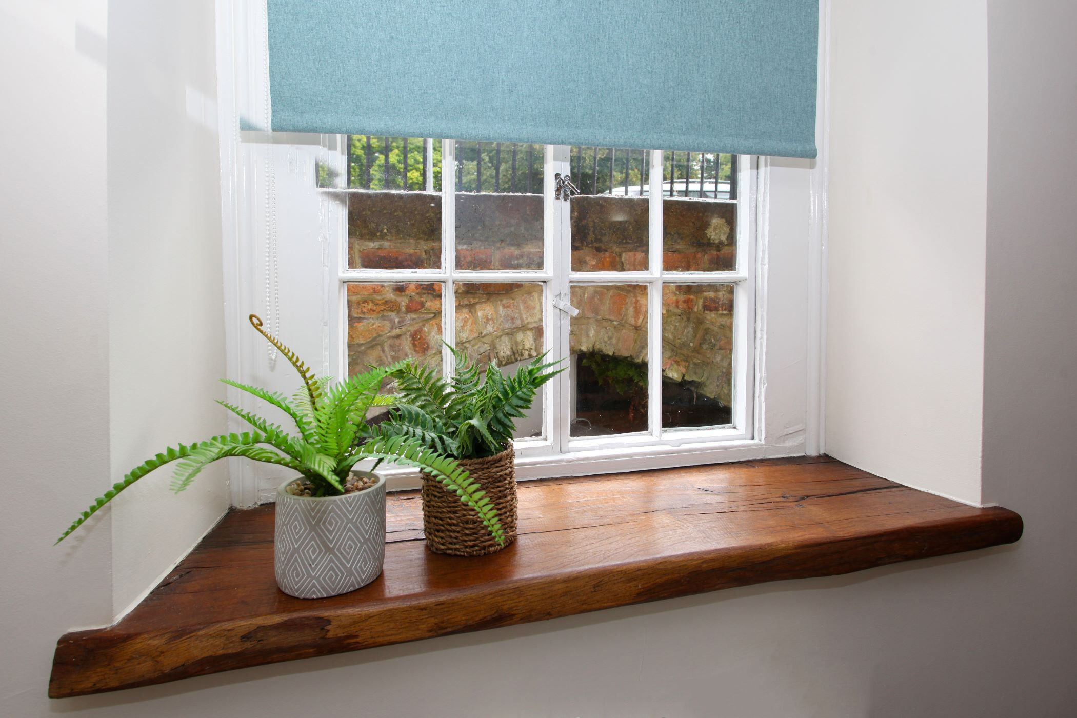 Une fenêtre avec un rebord en bois, deux plantes en pot et un rideau bleu.