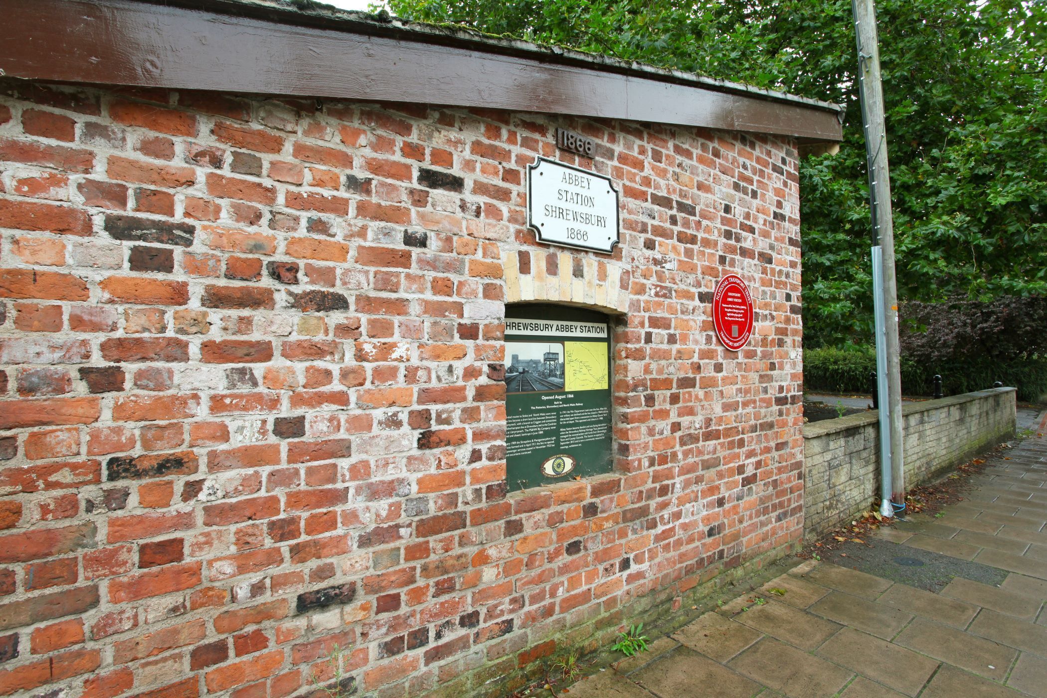 Eine Ziegelwand mit einer Plakette und einem roten Hinweisschild.