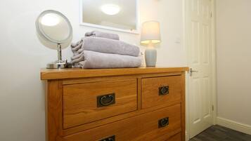 A wooden dresser with a round mirror, a lamp, and folded towels.