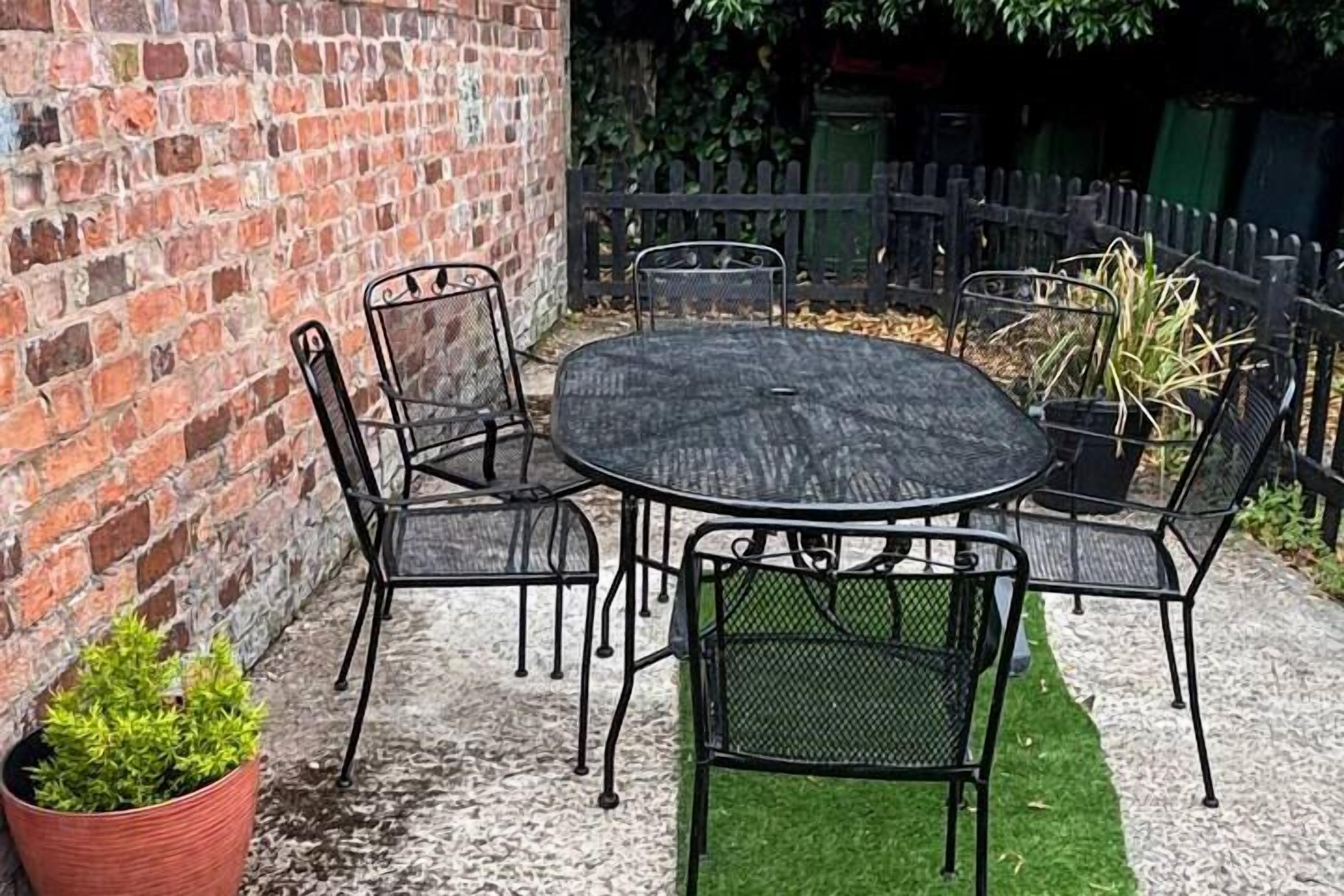 Een terras met een ronde tafel en zes stoelen, omringd door een bakstenen muur en een houten hek.