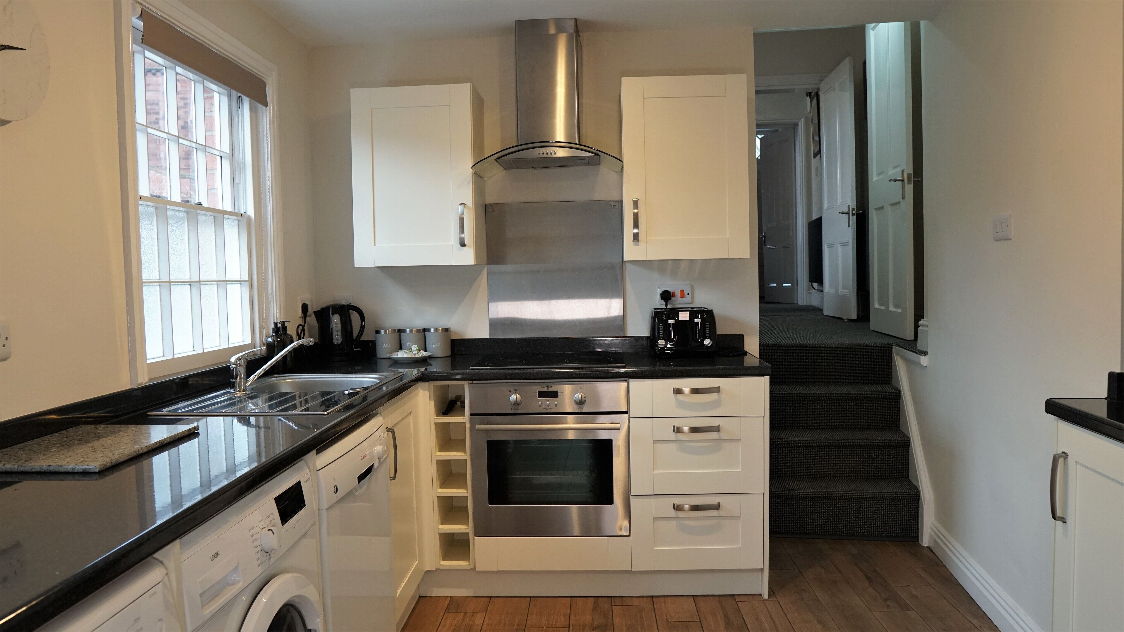 Una cocina compacta con estufa de acero inoxidable, horno empotrado, lavadora y cafetera.