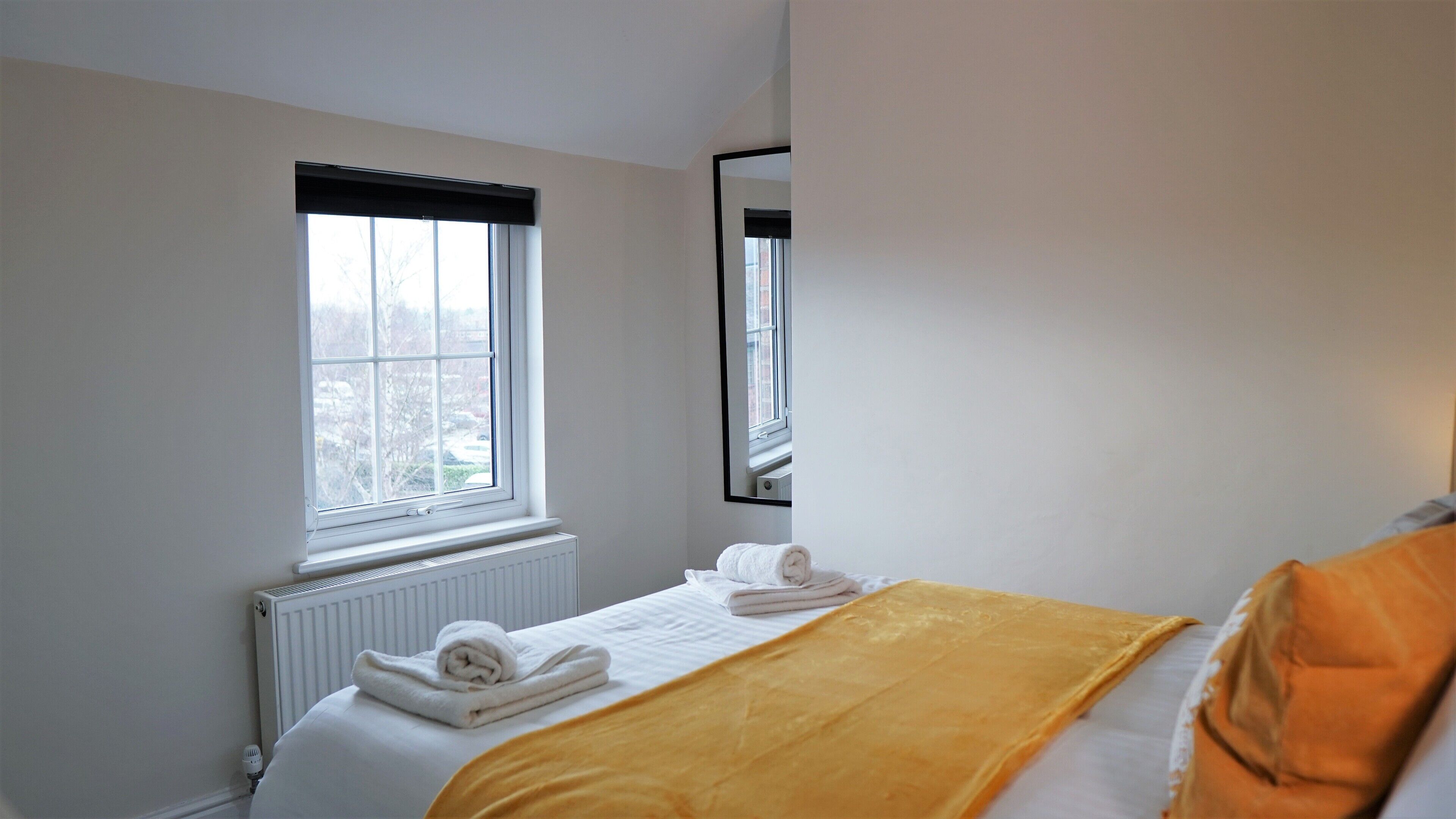 Una habitació d'hotel amb un llit, una finestra amb persianes, un radiador i un mirall a la paret.