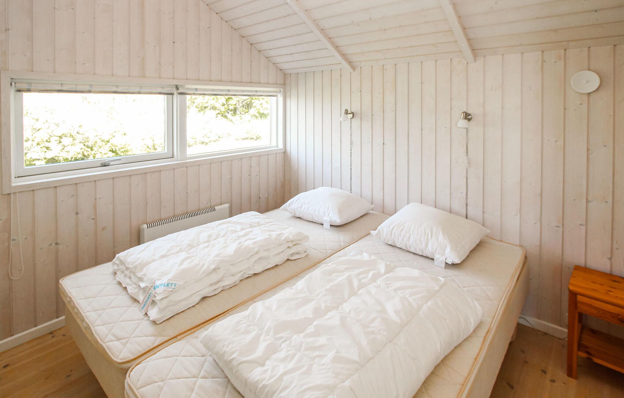 Een kamer met twee bedden, houten wanden, een raam en een klein houten tafeltje.