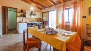 Un coin repas avec une table dressée pour deux personnes, une cuisine en arrière-plan et une vue sur l’extérieur par une fenêtre.