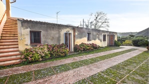 Un bâtiment rustique, avec un chemin de briques menant à une porte, entouré d’une végétation luxuriante et sous un ciel dégagé.