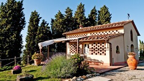 Un pequeño edificio con techo de tejas, pared con diseño de cuadros y un patio con mobiliario exterior.