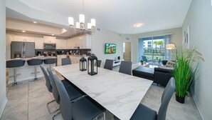 A modern kitchen with white cabinets, a large island, and a dining area with a marble table and black chairs.