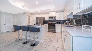A modern kitchen with white cabinets, a central island with bar stools, stainless steel appliances, and a backsplash of black tiles.