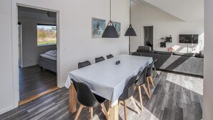 A modern, well-lit room with a dining table, chairs, and a sofa. There is a bed in the adjacent room, and a TV mounted on the wall. - 3 bedroom gorgeous home in Samsø (Samsø)