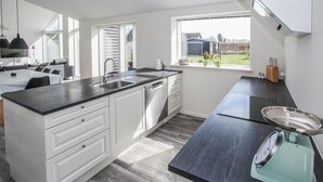 A modern kitchen with white cabinets, a black countertop, and a window with a view of a house and trees. - 3 bedroom gorgeous home in Samsø (Samsø)