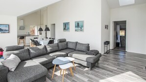 A modern living room with a grey sectional sofa, a small round table, and a dining area with a white table and chairs. - 3 bedroom gorgeous home in Samsø (Samsø)