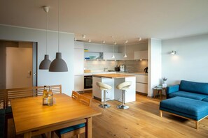 Una cucina moderna con isola centrale, sgabelli da bar, luci a sospensione e un divano blu in zona soggiorno.