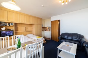 Un espacio habitable compacto con kitchenette, una zona de comedor con mesa y sillas, una cama, un sofá de cuero negro y un televisor.