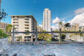 A gated outdoor area with a stone-tiled floor, surrounded by modern buildings and palm trees.