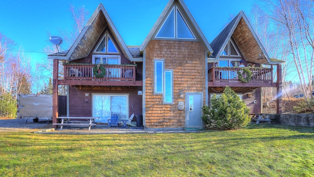 A two-story wooden house with a balcony on the upper floor, a front door, and a small front yard. - 7 Grandview - Unit D - Great condo close to downtown Rangeley (Rangeley)