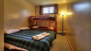 A bunk bed with a plaid bedspread and towels, a window with curtains, and a floor lamp. - 7 Grandview - Unit D - Great condo close to downtown Rangeley (Rangeley)
