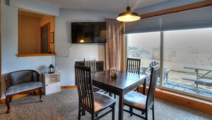 A dining area with a wooden table and chairs, a television mounted on the wall, and a large window with a view of the outside. - 7 Grandview - Unit D - Great condo close to downtown Rangeley (Rangeley)
