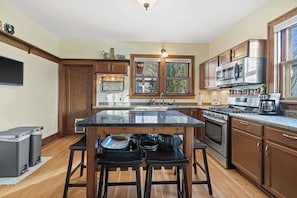 Une cuisine avec des meubles en bois, un îlot central doté de tabourets, un four à micro-ondes, une cuisinière et une grande fenêtre.