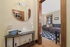 Un couloir avec un grand miroir rond, un panneau d’accueil, une console dont le plateau est en verre et un parquet en bois foncé.