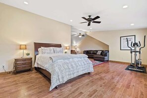 Une chambre à coucher comprenant un lit, une table de chevet, une lampe, un ventilateur de plafond, un tapis de course et un tableau encadré accroché au mur.