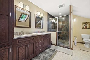 Ein Badezimmer mit einem Doppelwaschbecken, einer Dusche mit Glastüren, einer Toilette und einem großen Spiegel.