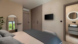 Une chambre à coucher moderne, équipée d’un lit, d’une télévision, d’un miroir et d’une salle de bain avec un lavabo.