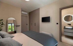 A modern bedroom with a bed, a television, a mirror, and a bathroom with a sink.
