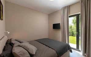 Een slaapkamer met een bed, een flatscreen televisie aan de muur en een schuifdeur naar een tuin.