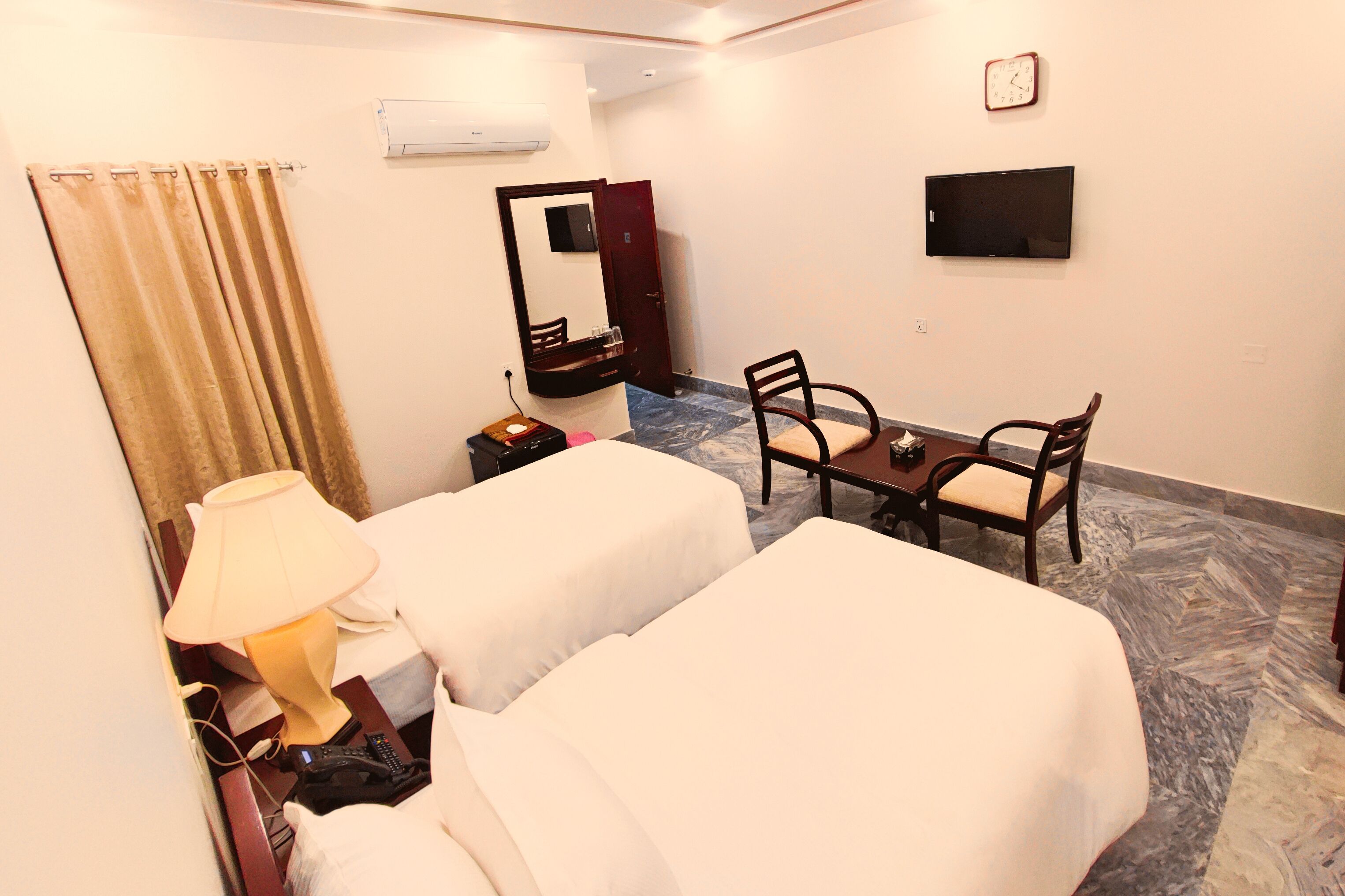 A hotel room with two beds, a desk with a chair, a TV, a mirror, and a lamp.