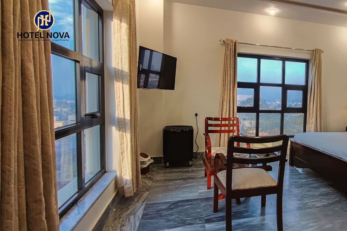 A hotel room with a bed, a chair, a desk with a lamp, a TV, and a window with curtains.
